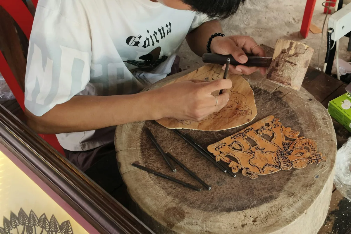 Manos trabajando una tabla de madera con herramientas de talla tradicionales sobre un banco de taller